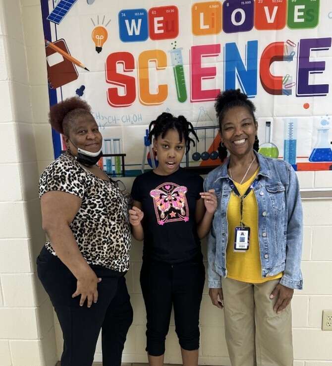 Cougar level student with teacher and paraprofessional in front of the science room