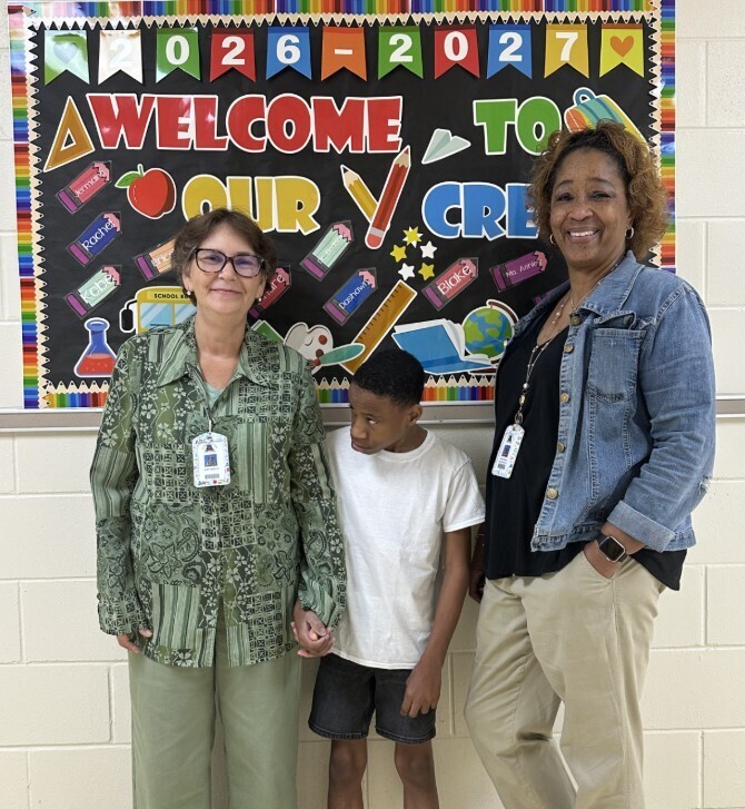 Jag level teacher, para, and student in front of welcome sign