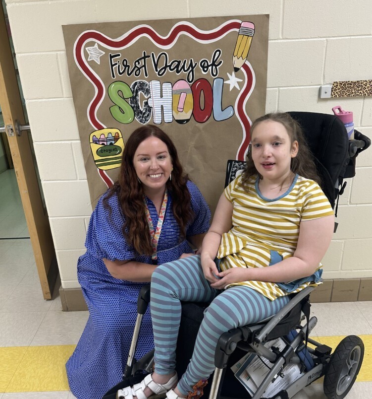 Cub level teacher with wheel chair student in front of first day of school sign