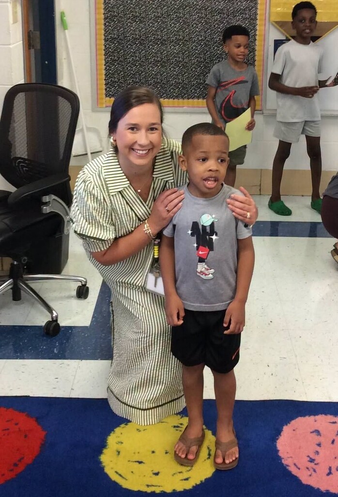 A teacher poses with a student in a classroom