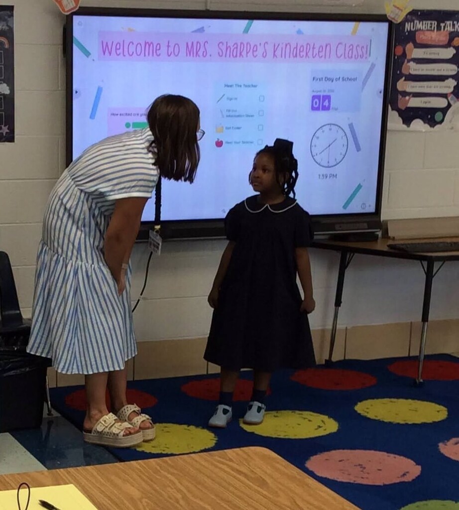 A teacher bends down to talk to a student in a classroom