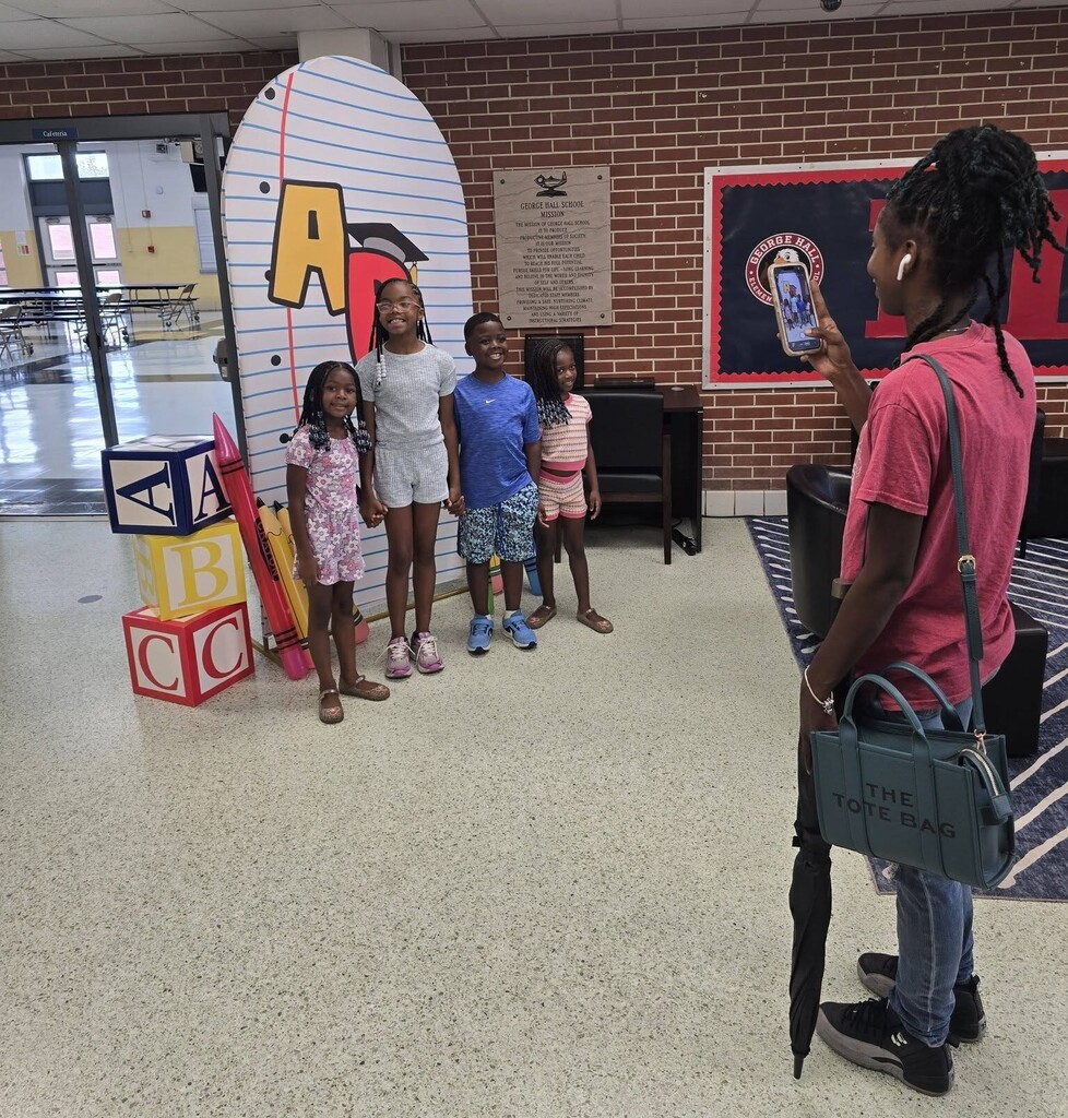 A parent takes a photo of four students in a school hallway