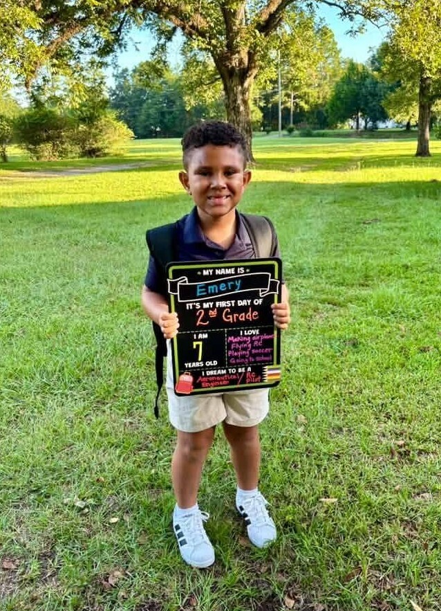 A boy standing outside holding a sign that reads "2nd Grade"