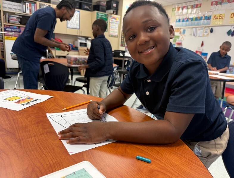 Student smiling at the camera while completing a work sheet