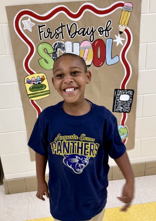 Cub level student smiling in front of first day of school sign
