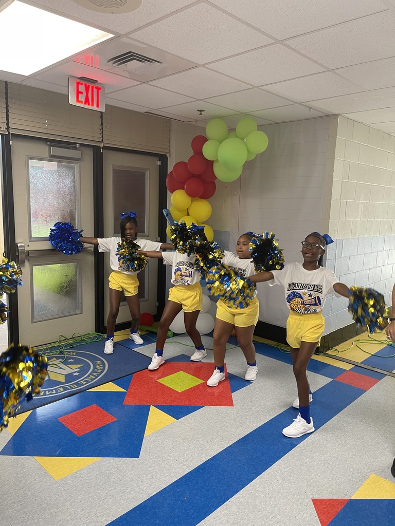 Four cheerleaders in matching uniforms perform a routine indoors with balloons in the background.