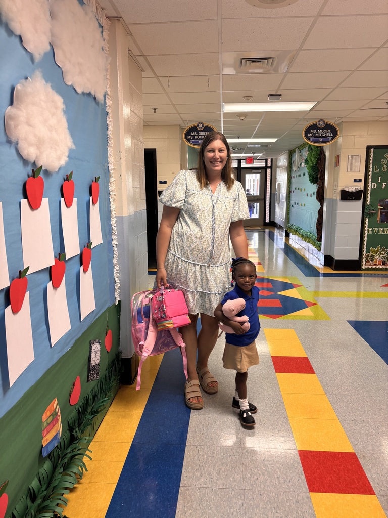 Woman and child walking in a hallway with decorative walls and colorful floor. The child holds a backpack.