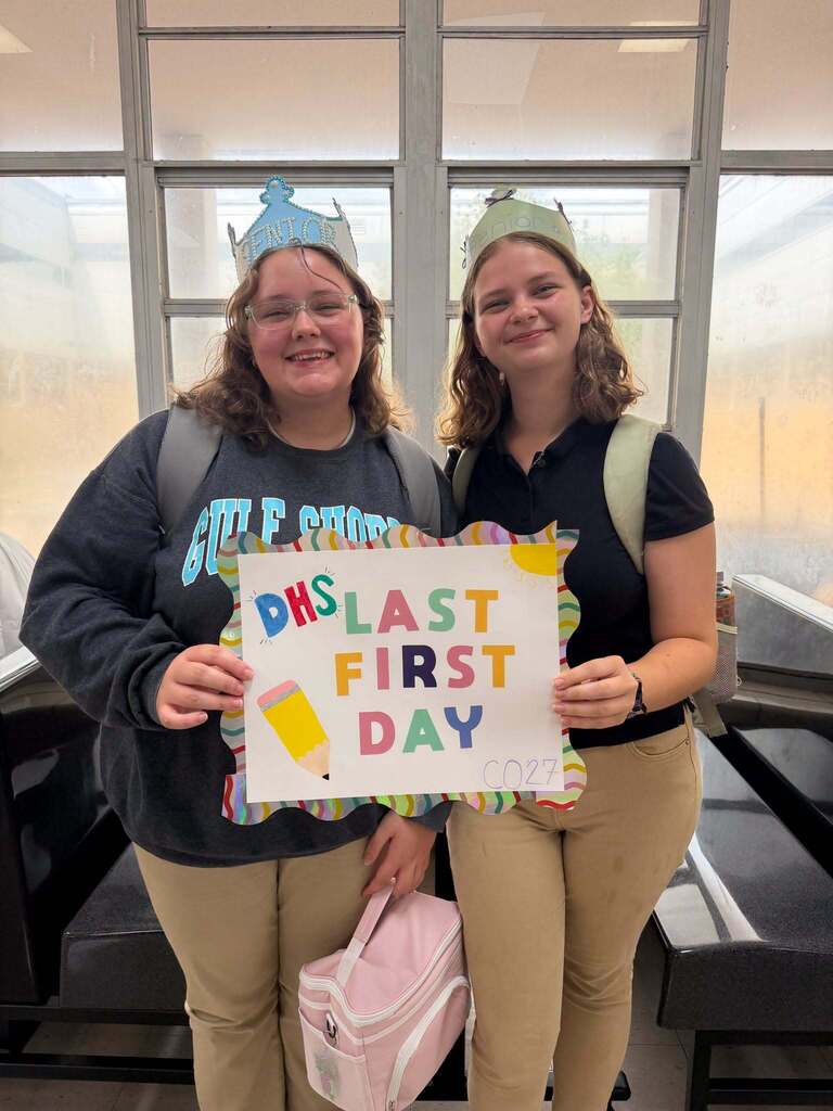 Two girls wearing paper crowns and holding a sign that reads "Last First Day"