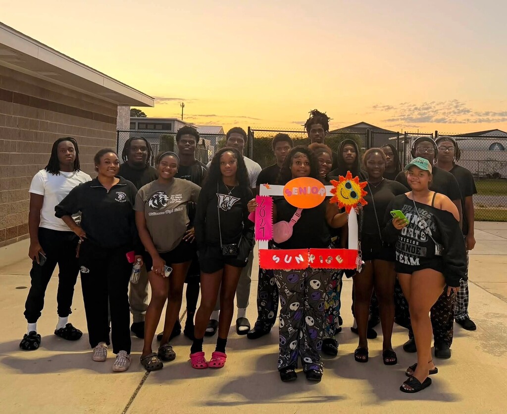 A group of students standing at a football stadium, holding a sign that reads "Senior Sunrise"