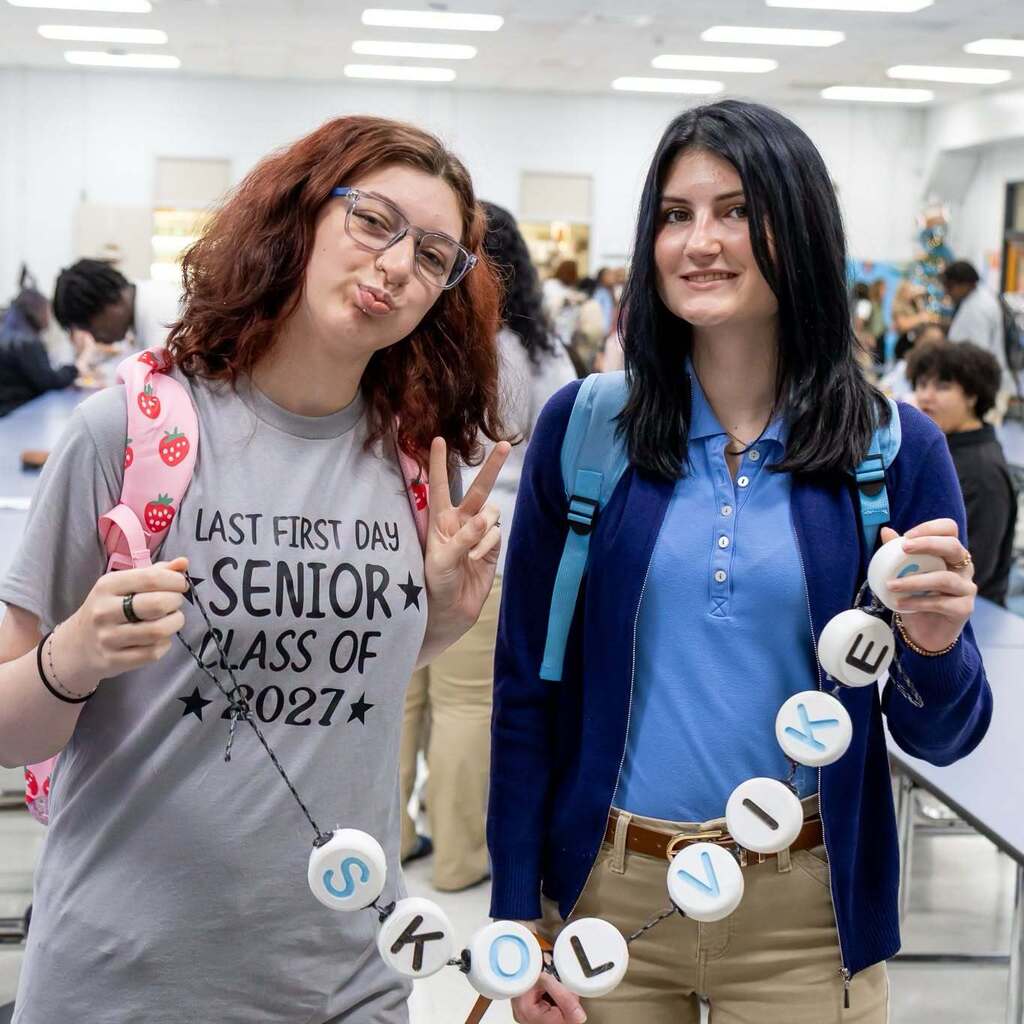 Two girls holding an oversized string of beads that reads "Skol Vikes"