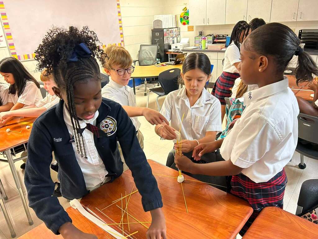 Four students building a tower base out of spaghetti noodles and marshmallows