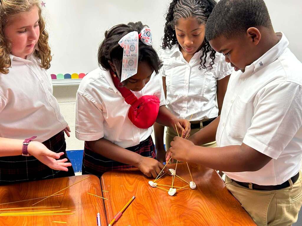 Four students building a tower out of spaghetti noodles and marshmallows