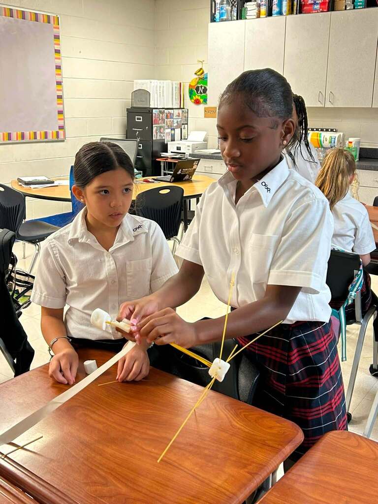 Two students building a tower base out of spaghetti noodles and marshmallows