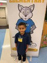 A young boy stands in front of a large banner featuring a cartoon wolf wearing a blue shirt and sneakers.