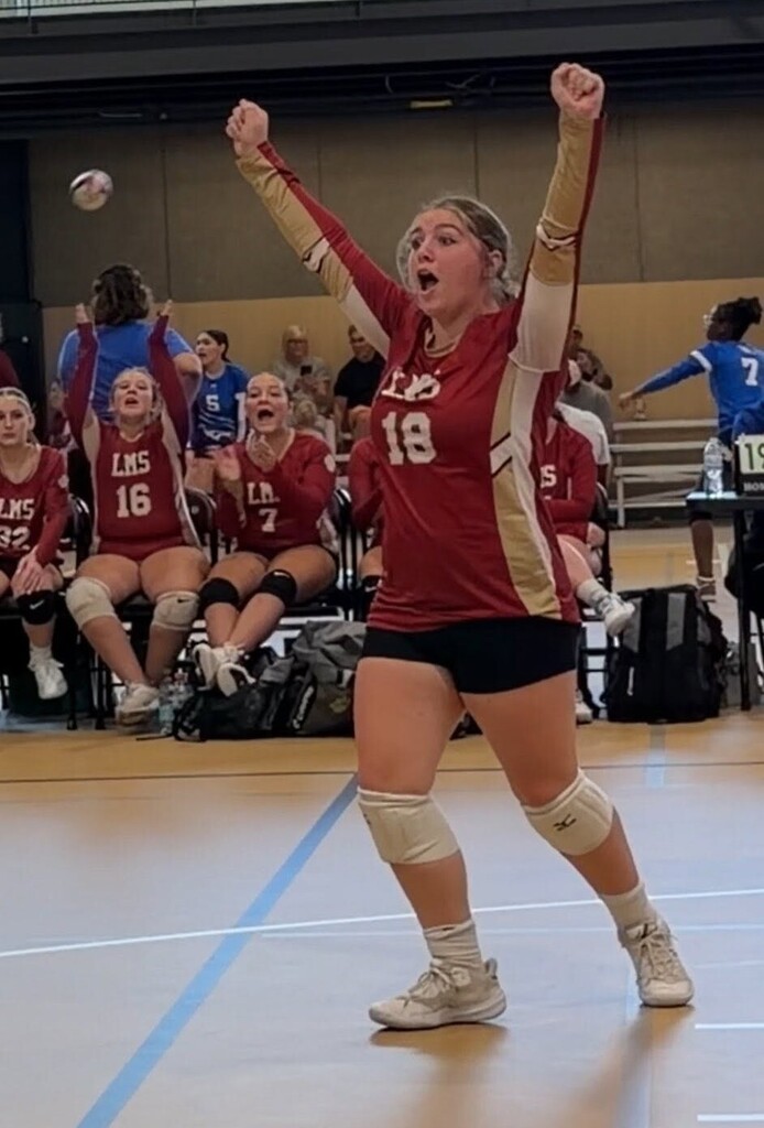 A volleyball player raises her arms in celebration on the court
