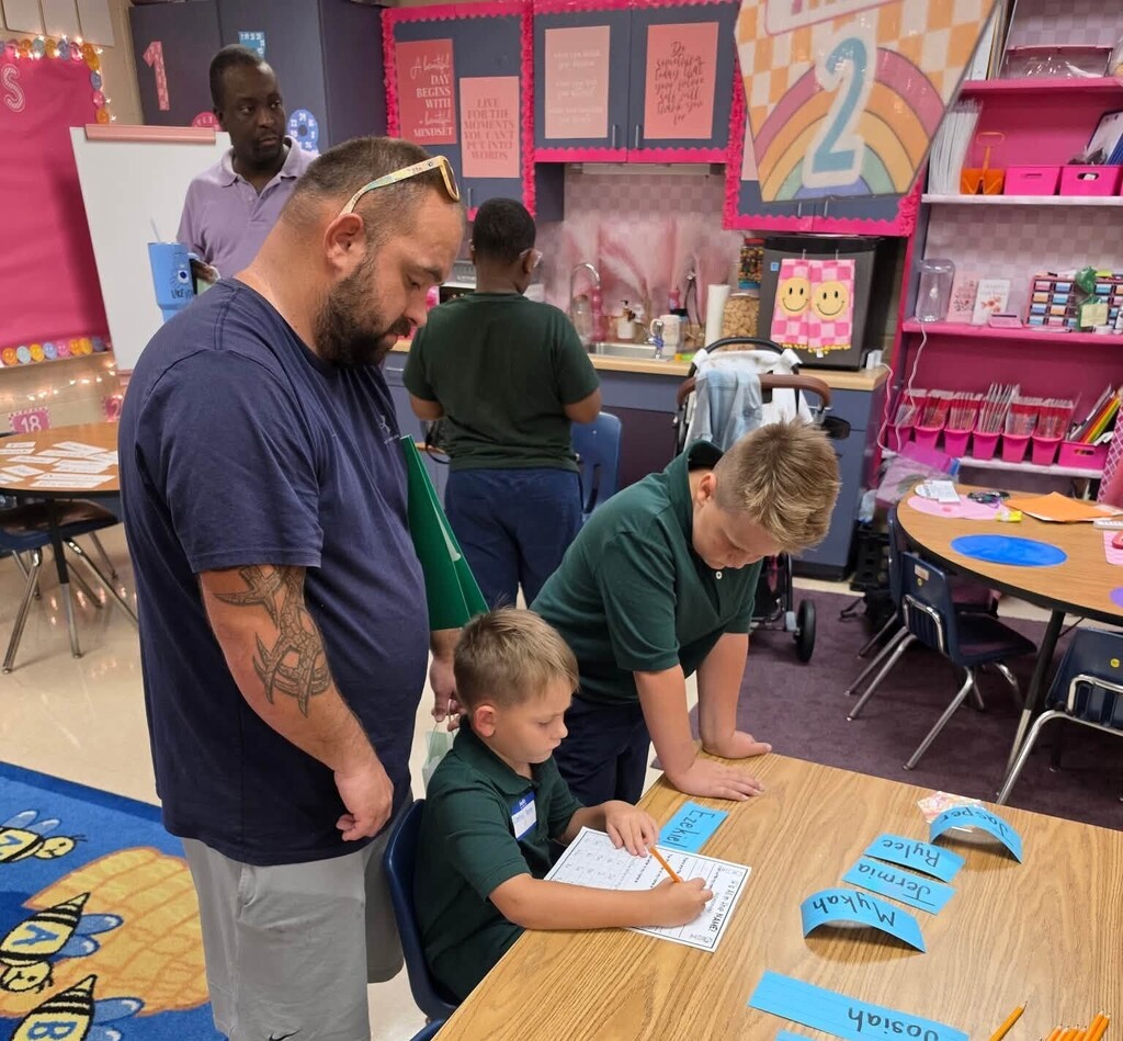 A dad and big brother look on as a young student writes on a worksheet