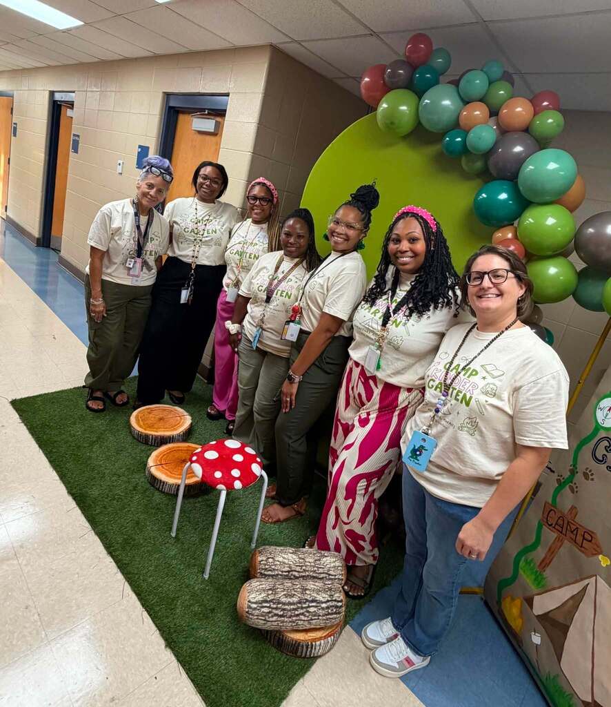 A group of teachers stand in a campground setting in school hallway