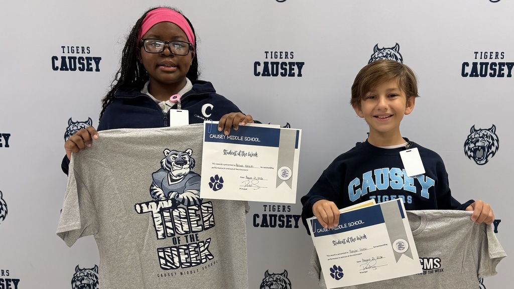 Two children hold up a certificate and a T-shirt. One wears a pink headband, and the other wears a black shirt.