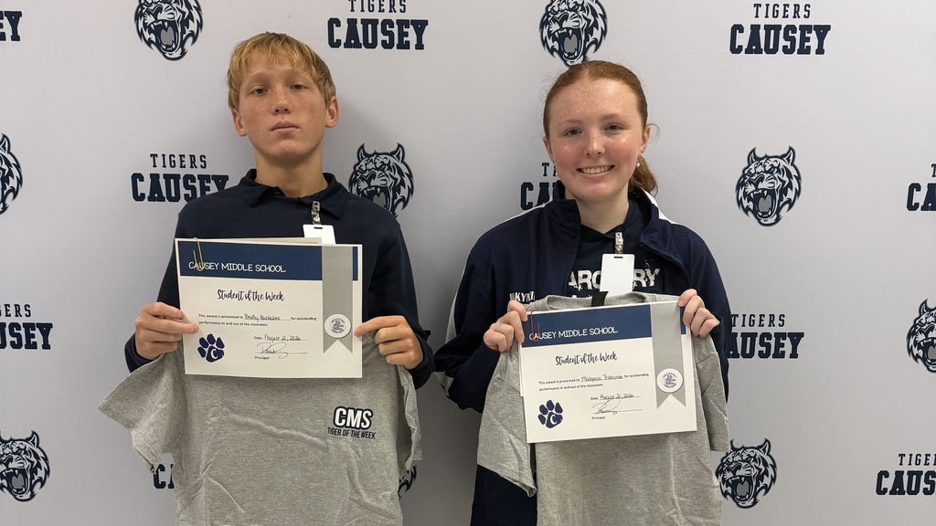 Two individuals in blue jackets hold certificates and gray T-shirts in front of a wall with the word "CAUSEY".