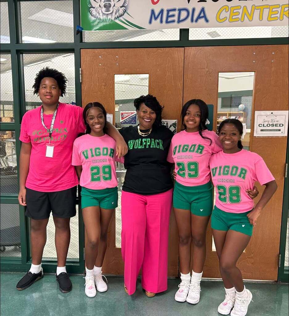 Four students wearing pink stand with a teacher who is wearing a shirt that reads "Wolfpack"