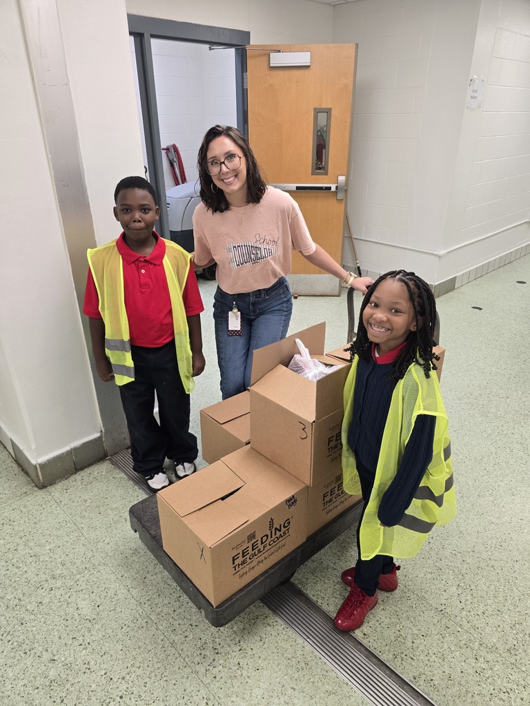 Three children in safety vests pose in front of boxes on a handcart. The setting appears to be a corridor.