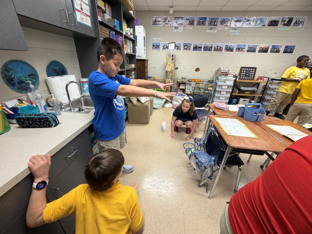 Three children in a classroom. One child holds out hands, another crouches, and the third reaches for a counter.