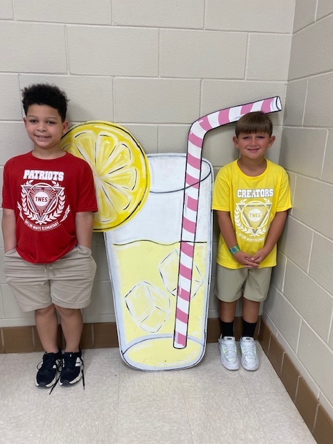 Two young boys stand next to a large paperboard cutout of a lemonade glass with a straw.