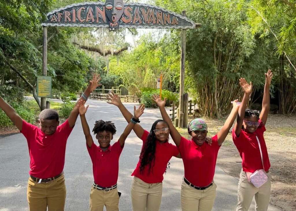 Five students in red shirts raising their arms at a zoo