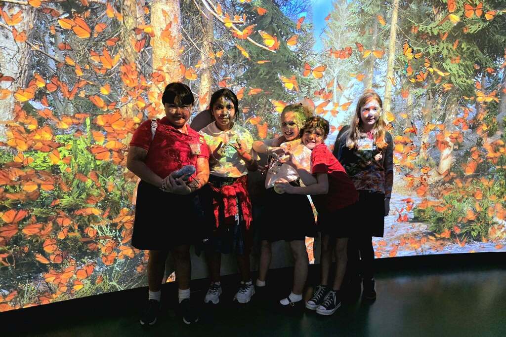 Five students standing in front of a projection screen filled with leaves