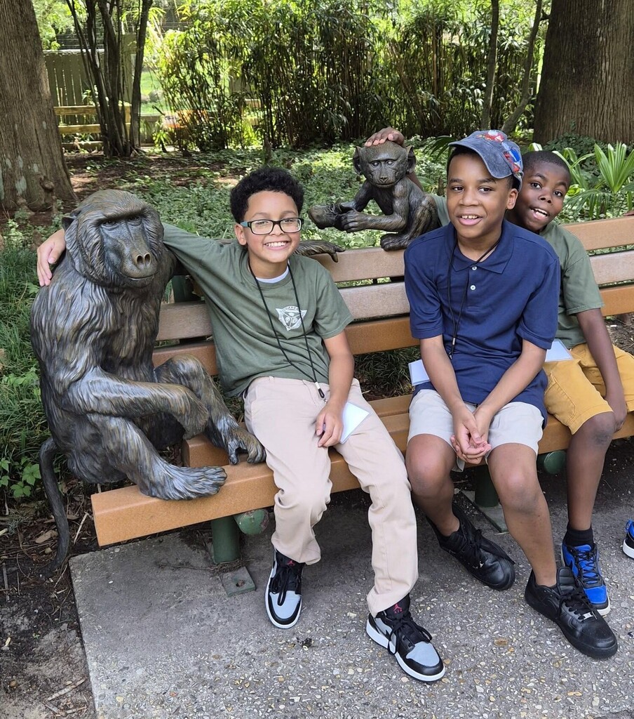 Three students sitting on a bench next to statues of monkeys
