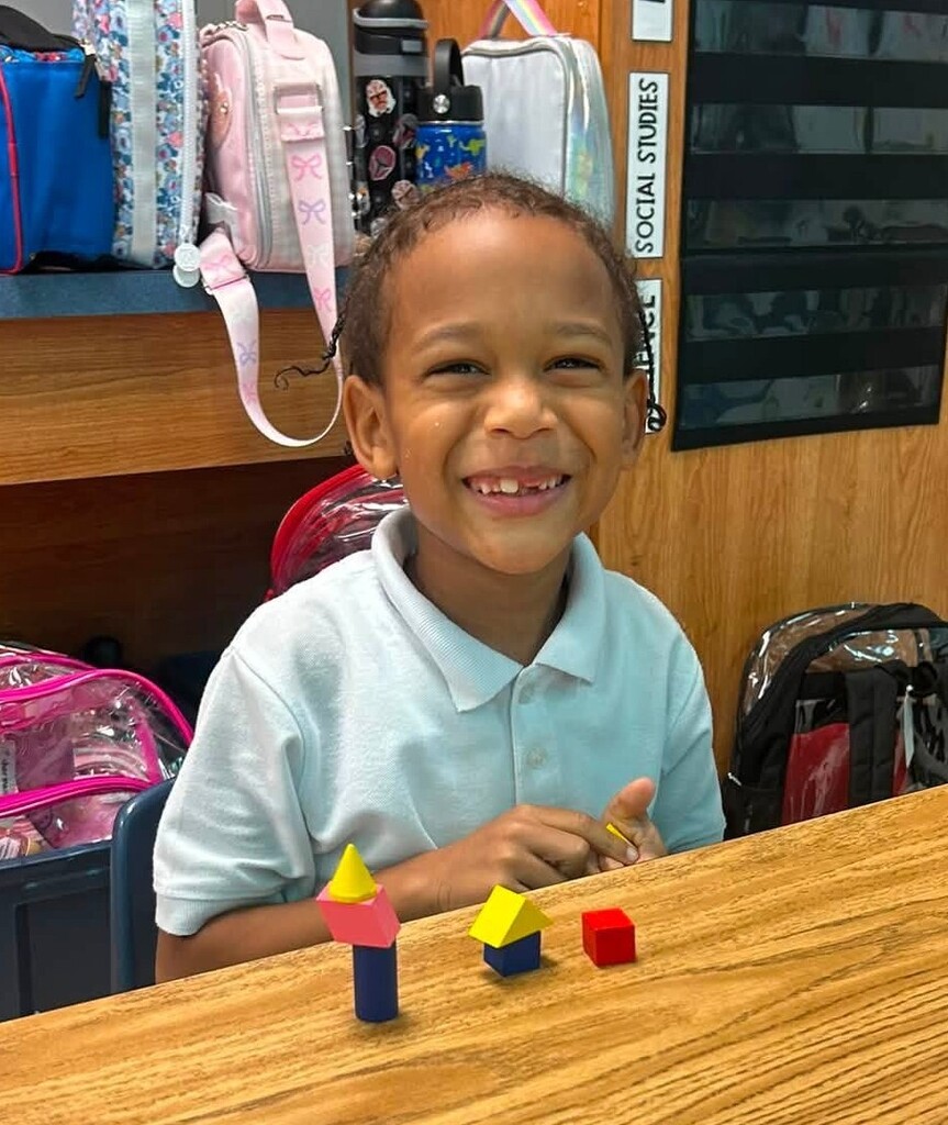 A smiling student with math manipulatives stacked on the table in front of her