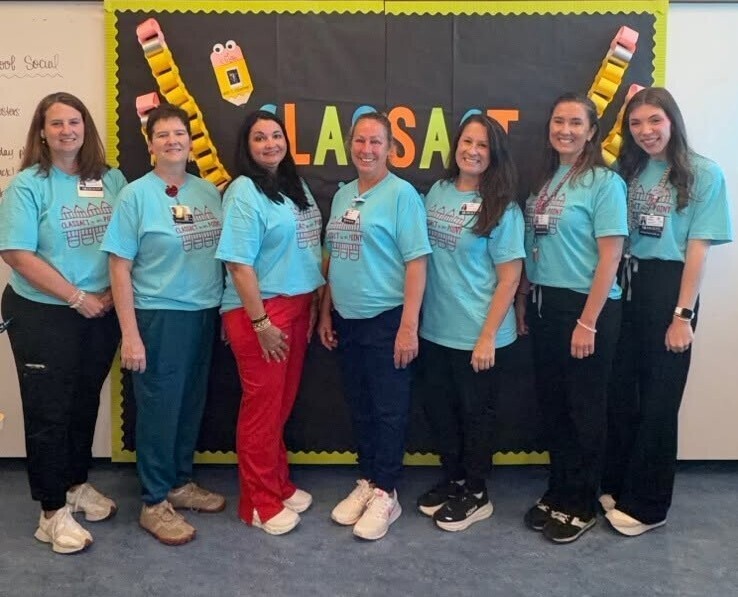 A group of seven teachers in teal T-shirts