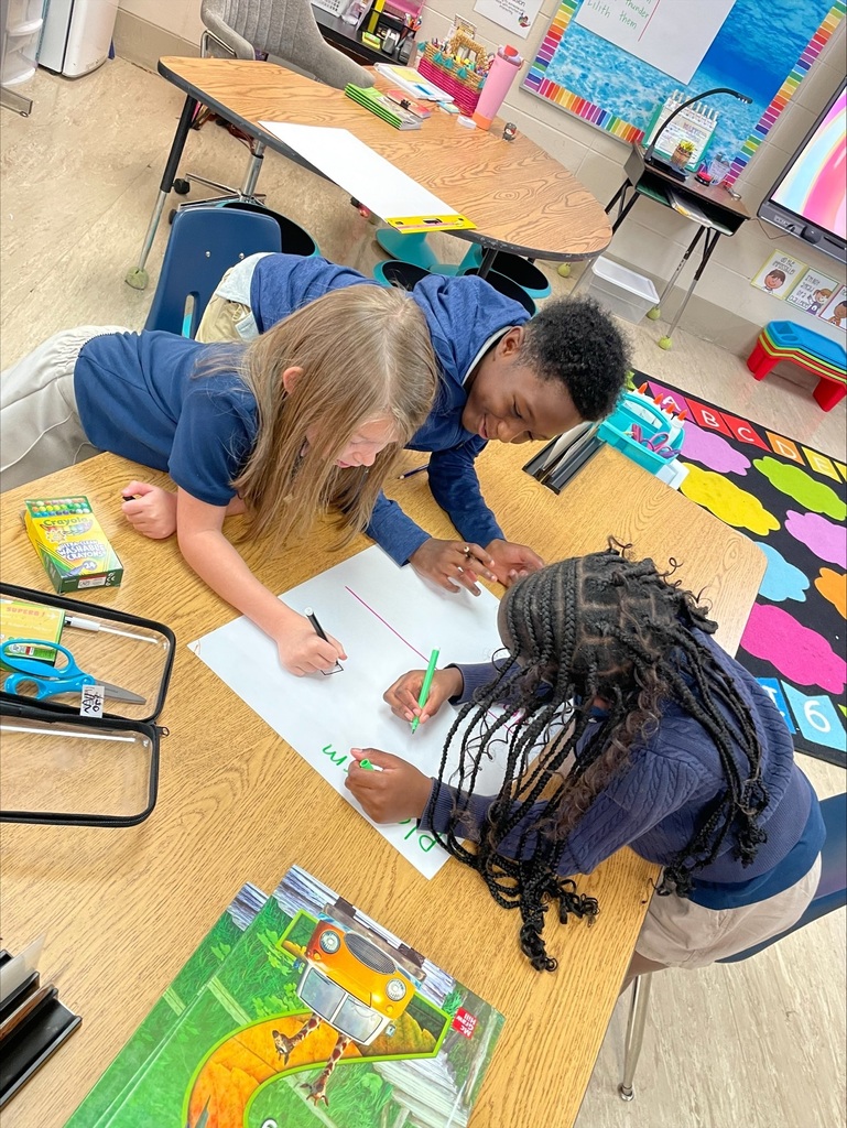 trio of students at a classroom table working on a poster together