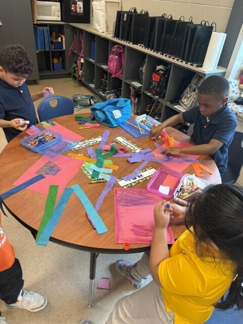 Kids sit at a table, creating artwork with colorful papers and craft materials in a classroom.