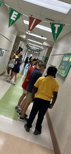 A hallway with students lined up, facing away from the camera, and banners with the letters E, T, and F hanging above.
