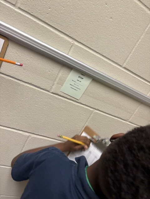 Person writing on a clipboard with a pencil. A note is attached to the wall above.