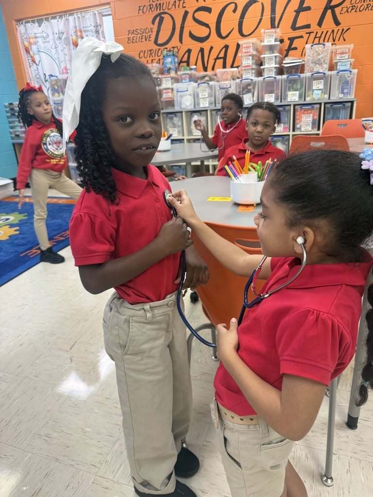 A girl with a stethoscope listens to another girl's heartbeat
