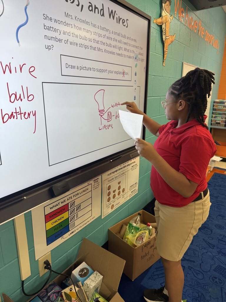A girl drawing a bulb and circuit on a smartboard