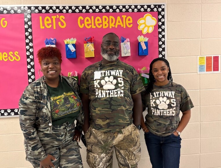 Three people, two women and one man, stand before a bulletin board that reads "Let's Celebrate".