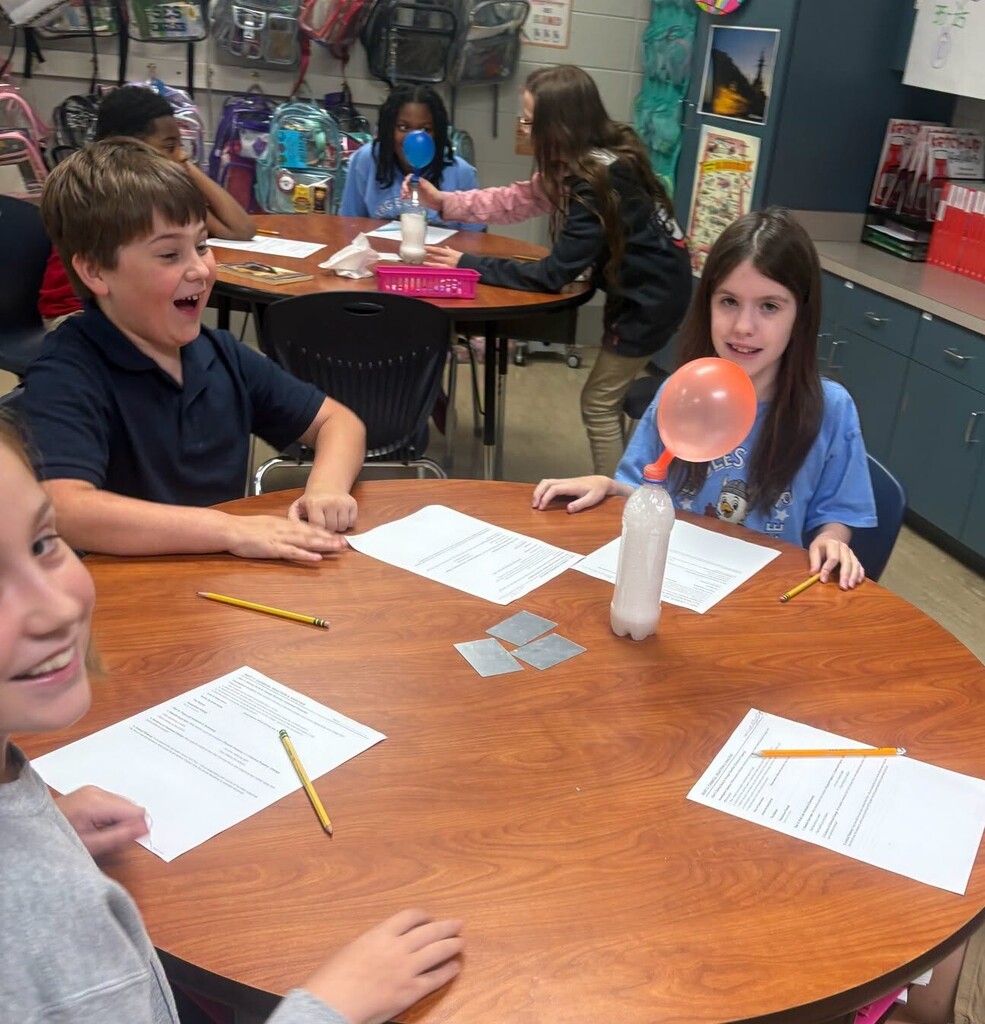 Three students at a table with a balloon in a water bottle