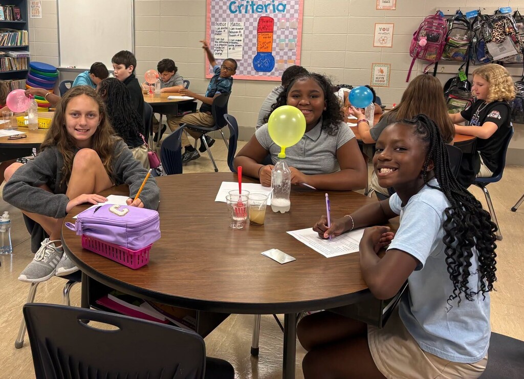 Three girls at a table with a balloon in a water bottle