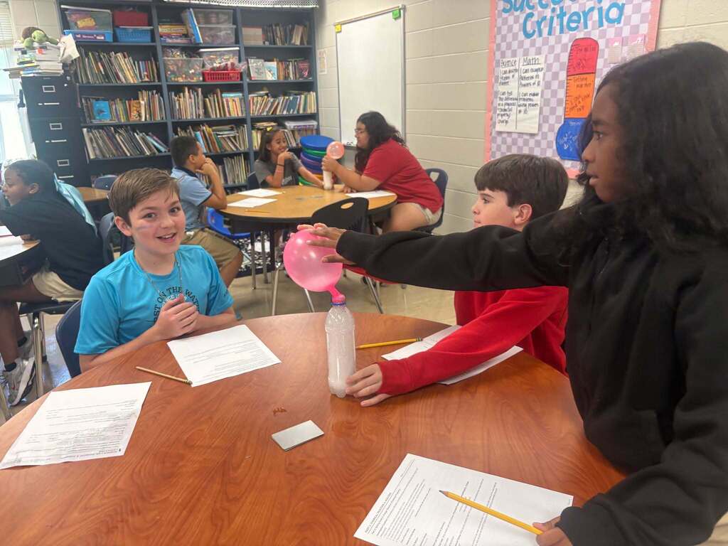 Three students at a table with a balloon in a water bottle
