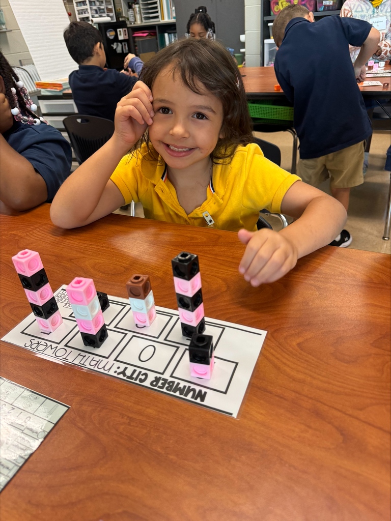 A young girl smiles while sitting at a table, playing a game of building blocks.