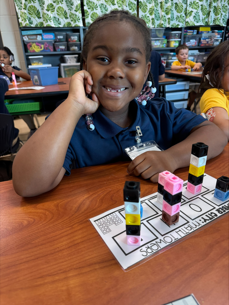 A young girl at a desk with a smile, engaged in an activity with colorful building blocks.