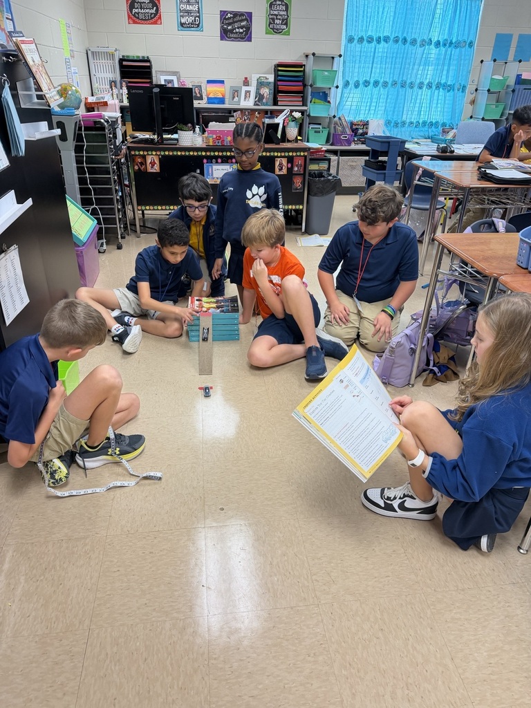 A classroom setting with students sitting on the floor, engaged in a hands-on activity, while others observe and interact.