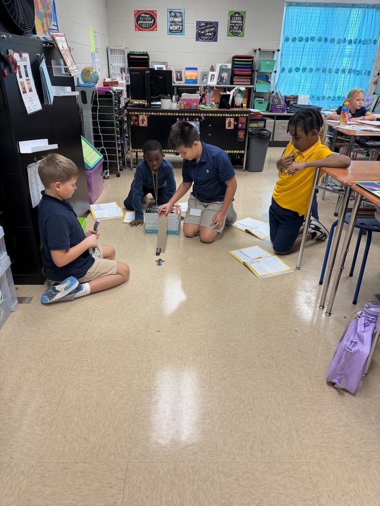 A group of children are sitting on the floor in a classroom, working on a project with materials.