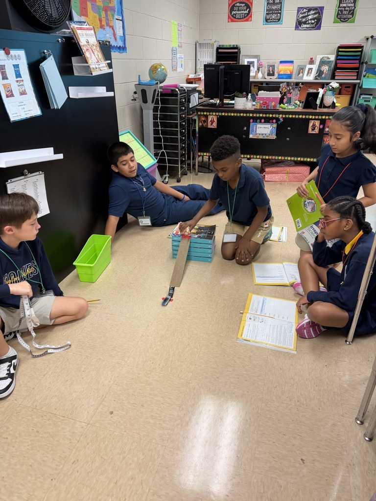 Five children in blue uniforms sit on a classroom floor, working with a book and a tool.