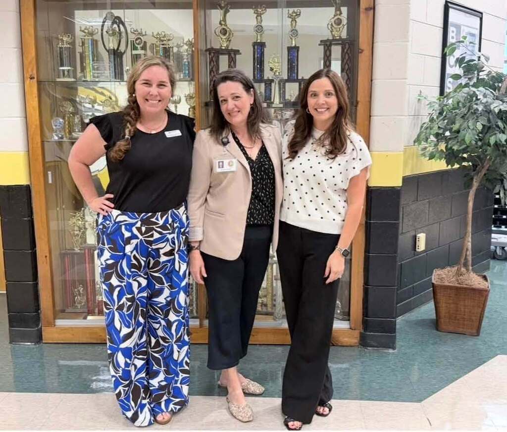 Three educators standing in front of a trophy caase