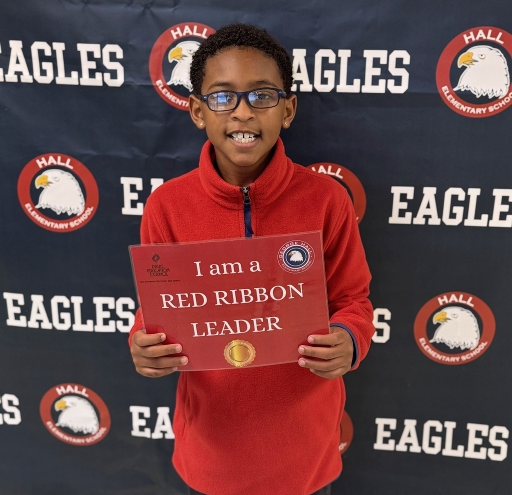 Child wearing red sweater and glasses holds a sign that reads "I am a RED RIBBON LEADER."