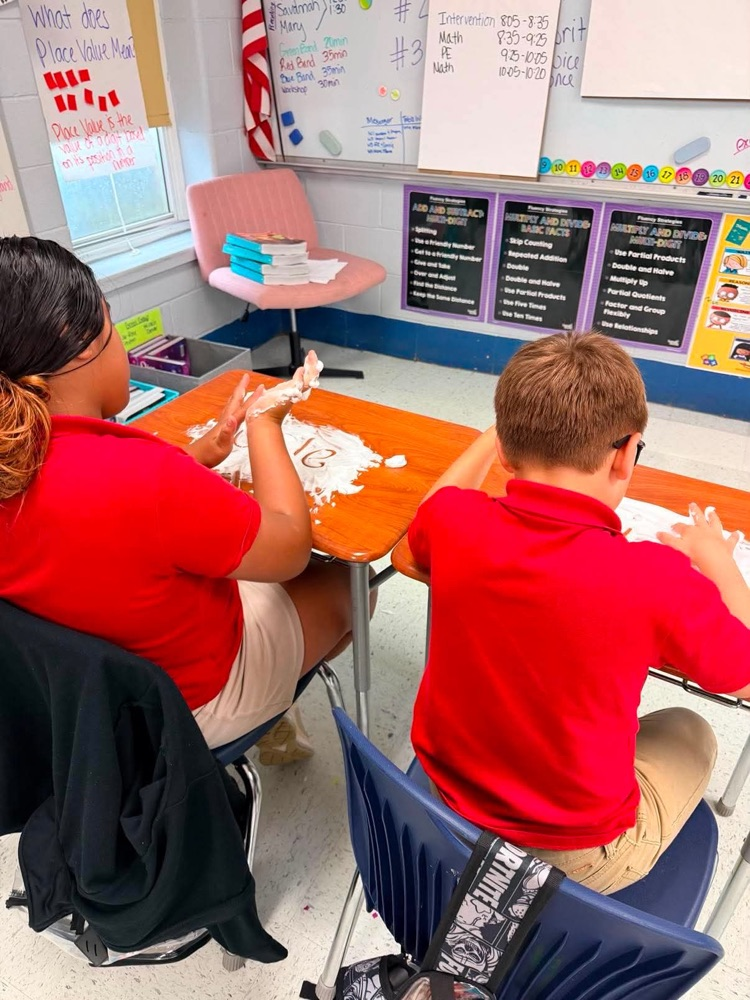 Mrs. Allen’s student writing spelling words in shaving cream on their desk in the classroom. 